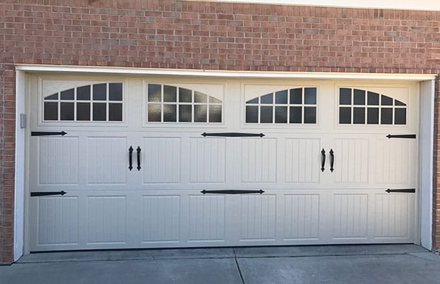 Closed white garage door with windows and brick wall.