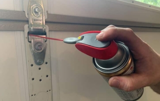 Hand holding lubrication for garage door hinge.