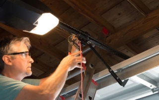 Closeup of a professional automatic garage door opener repair service technician man working on a ladder at a home residential location making adjustments and fixing it while installing it.