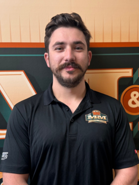 A man with short dark hair and a mustache wears a black M&M Enterprises polo shirt, standing in front of a matching company logo background. | M&M Garage Doors