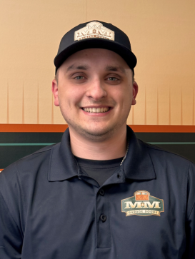 A man in a navy polo shirt and matching cap with a logo stands and smiles in front of a tan and orange background. | M&M Garage Doors