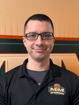 A person with short dark hair and glasses wearing a black polo shirt with an "MM Career Group" logo stands in front of a matching logo background. | M&M Garage Doors