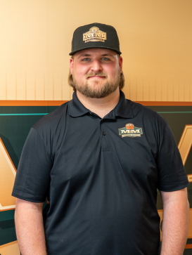 A man with a beard wears a black cap and navy polo shirt with an "M&M Construction" logo, standing in front of a matching logo backdrop. | M&M Garage Doors