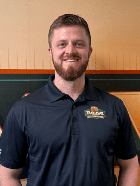 A man with short hair and a beard, wearing a dark polo shirt with an "MVM" logo, stands in front of an orange and green background, smiling at the camera. | M&M Garage Doors