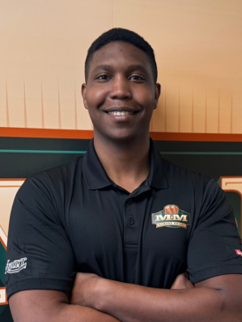 A person stands smiling with arms crossed, wearing a black MMM Construction polo shirt, in front of an orange and green logo background. | M&M Garage Doors