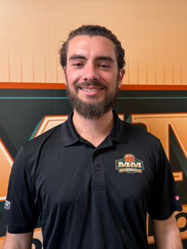 A man with dark hair and a beard wearing a black MM logo polo shirt stands smiling in front of an orange and green MM-themed background. | M&M Garage Doors