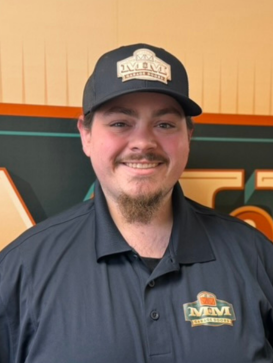 A man in a dark polo shirt and cap with a matching MVM logo stands smiling in front of a sign with the same logo. | M&M Garage Doors