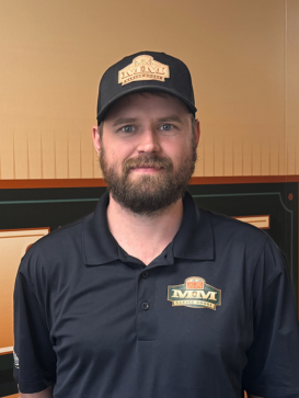Man with a beard wearing a black M&M-branded cap and polo shirt stands in front of a brown and black background. | M&M Garage Doors