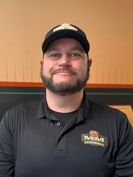 Man in a black MGM-branded polo and hat stands in front of a wall with an orange and green design, smiling at the camera. | M&M Garage Doors